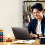 Asian author working on a laptop beside a stack of books showing the publishing steps from idea to success.